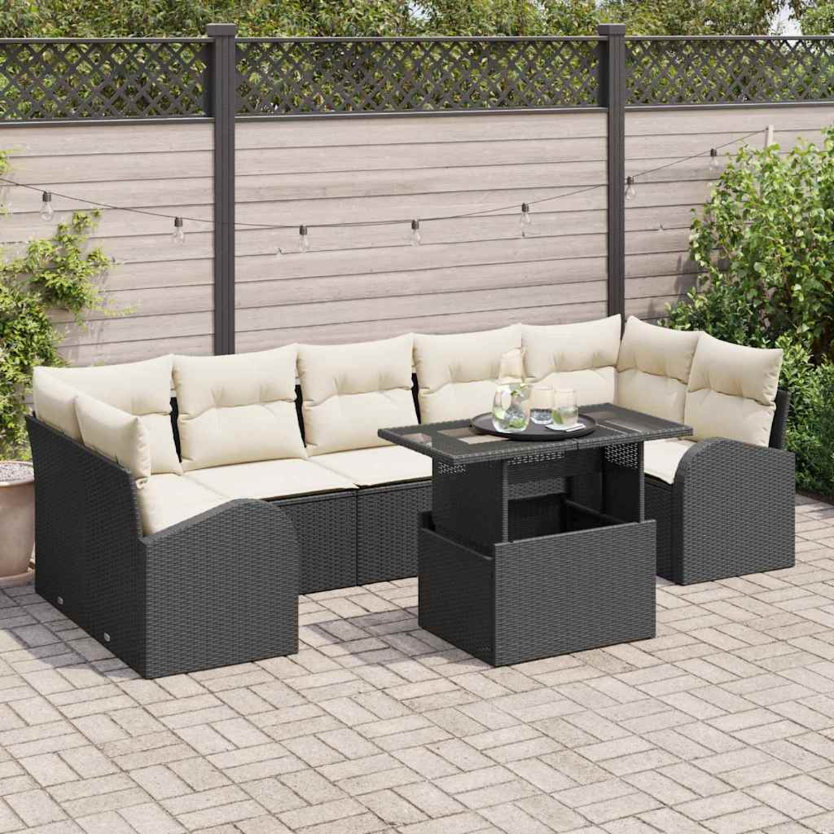 Garten-Set mit dunkelgrauem Korbsessel, cremefarbenen Kissen und einem Tisch mit Hubfunktion. Im Hintergrund sind ein Zaun und Pflanzen.
