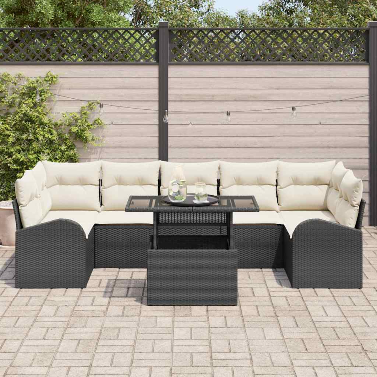 Outdoor-Terrassenset mit grauen Korbmöbeln, beigen Kissen und einem Tisch mit Glasplatte. Vor einem Holzzaun, Lichterketten und Grün.