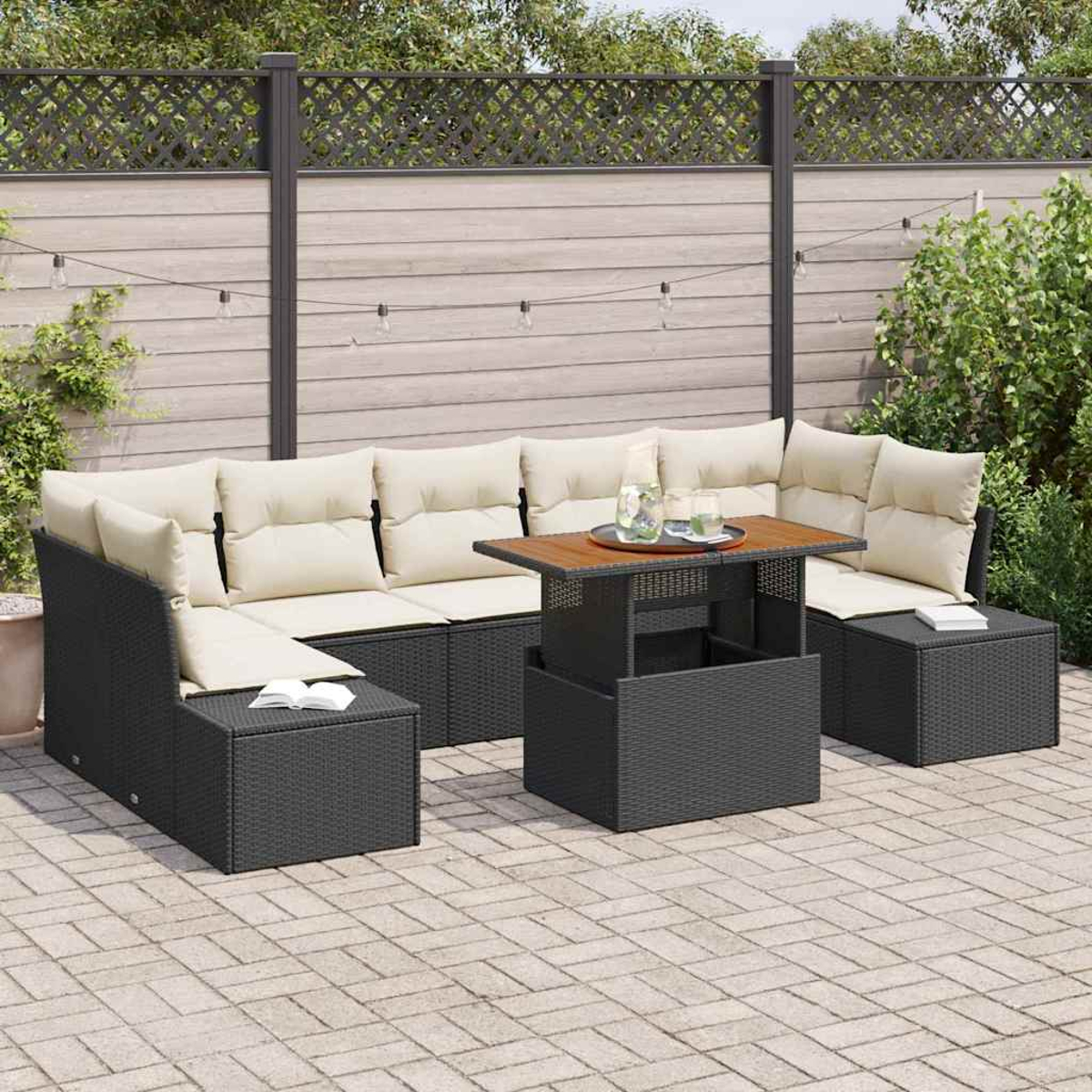 Gartenmöbel-Set mit schwarzem Korbgeflecht und cremefarbenen Kissen. Ein Holztisch mit Getränken steht in der Mitte. Ein Zaun im Hintergrund.