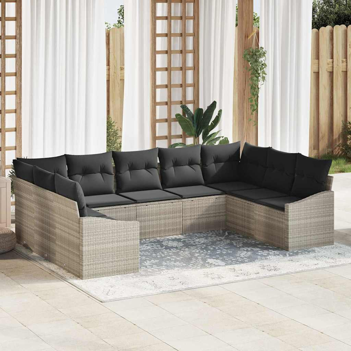 Ein U-förmiges Outdoor-Sofa mit schwarzen Kissen steht auf einer Terrasse. Weiße Vorhänge und ein Holzzaun sind im Hintergrund.