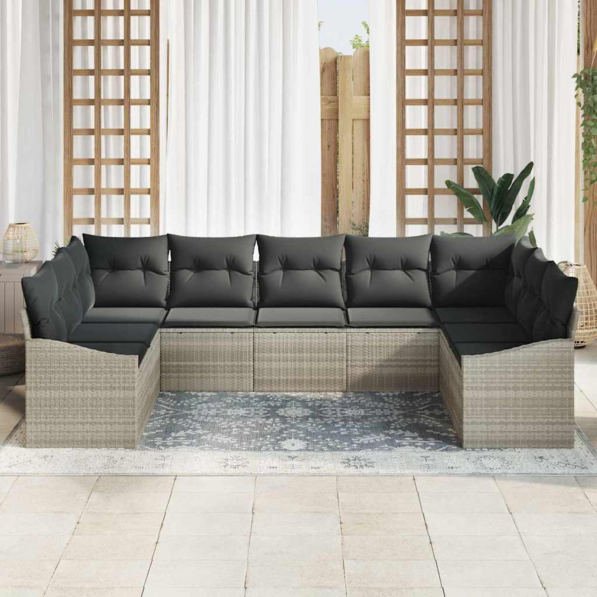 Outdoor-Ecksofa mit grauen Kissen, auf einem gemusterten Teppich, vor durchsichtigen Vorhängen und einem Holzgitter.