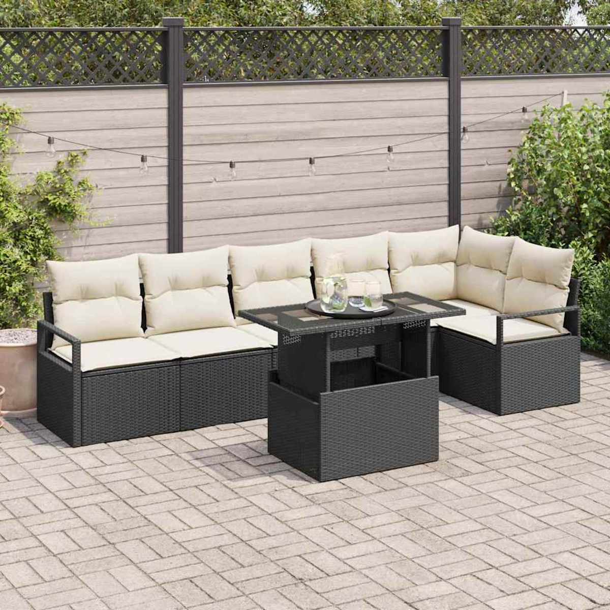 Juego de asientos al aire libre con cojines beige y una mesa elevable en un patio pavimentado. Una valla y vegetación al fondo.
