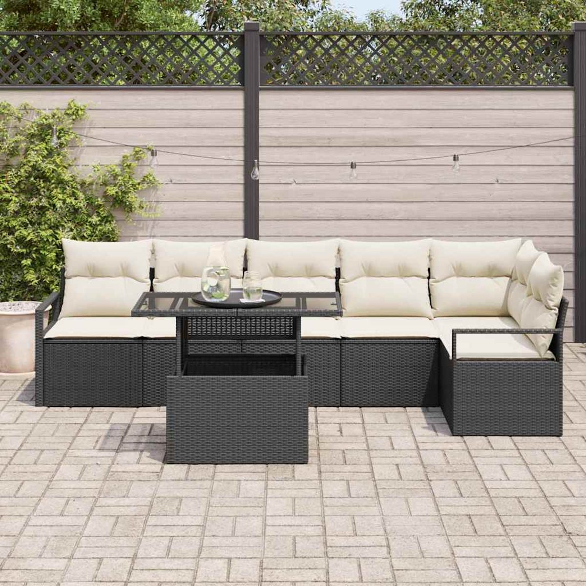 Sofá seccional al aire libre con cojines crema y una mesa negra. En un patio con valla de madera y luces de cadena al fondo.
