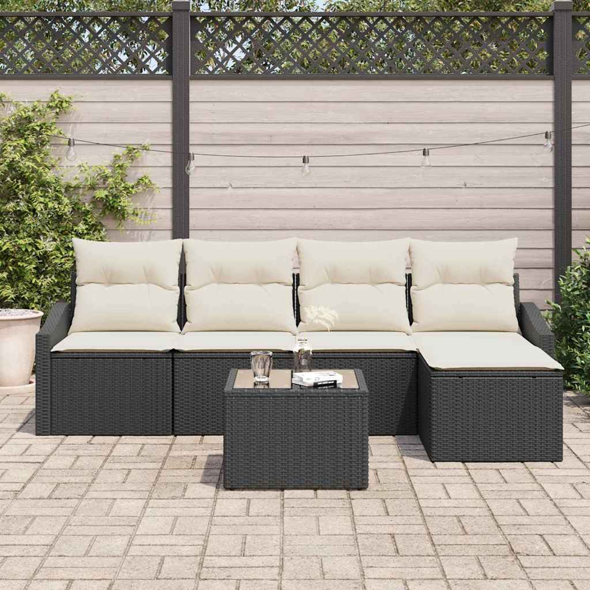 Gartenmöbel-Set mit schwarzem Korbsessel und passendem quadratischen Tisch, cremefarbenen Kissen, vor einem Zaun.