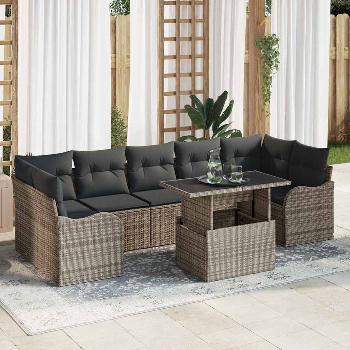 Terrassenset: Rattansofa mit schwarzen Kissen, Tisch mit Gläsern und Wasserkrug, auf einem Teppich und weißen Vorhängen.