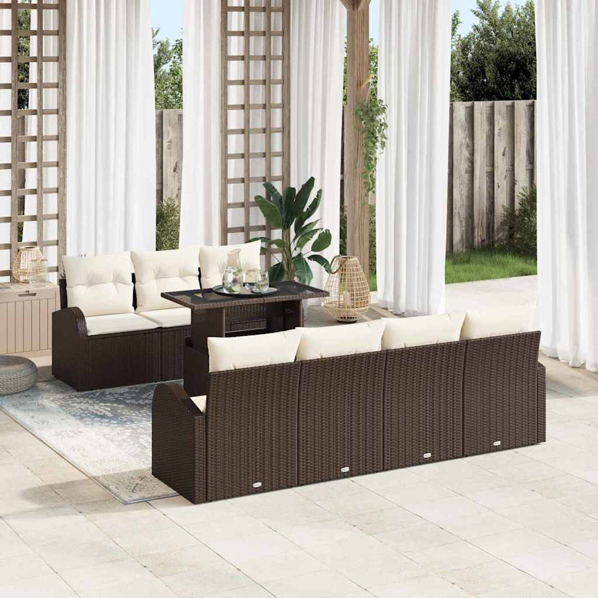 Terrassengarnitur mit braunen Korbs Sofas, beigen Kissen, Glastisch, weißen Vorhängen und üppigem Grün im Hintergrund.