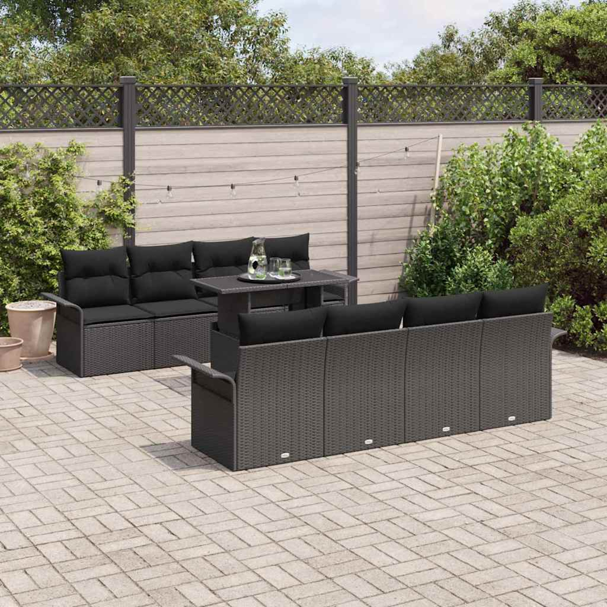 Terrassenset im Freien mit dunkelgrauen Korbsesseln, schwarzen Kissen, kleinem Tisch und Holzzaun im Hintergrund.
