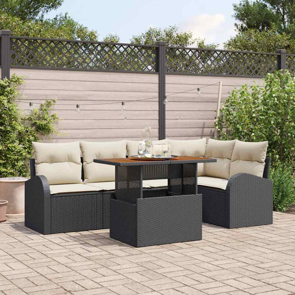 Terrassenmöbel-Set mit schwarzem Korbmöbel, beigen Kissen und einem Holztisch. Ein Zaun und Grün im Hintergrund.