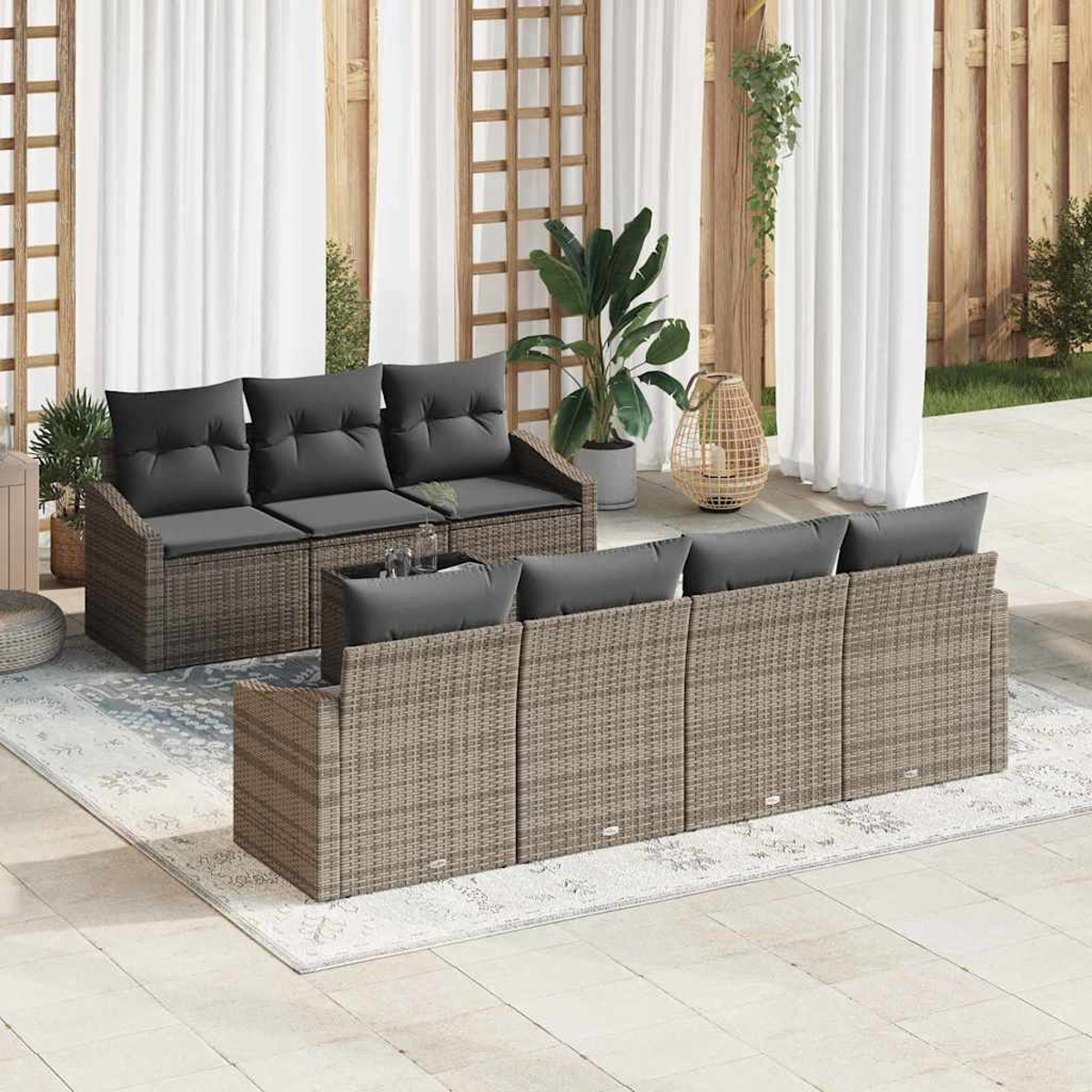 Terrassenset im Freien mit Korbmöbeln, grauen Kissen und einem Teppich. Der Hintergrund hat Pflanzen, Vorhänge und Holzzaun.