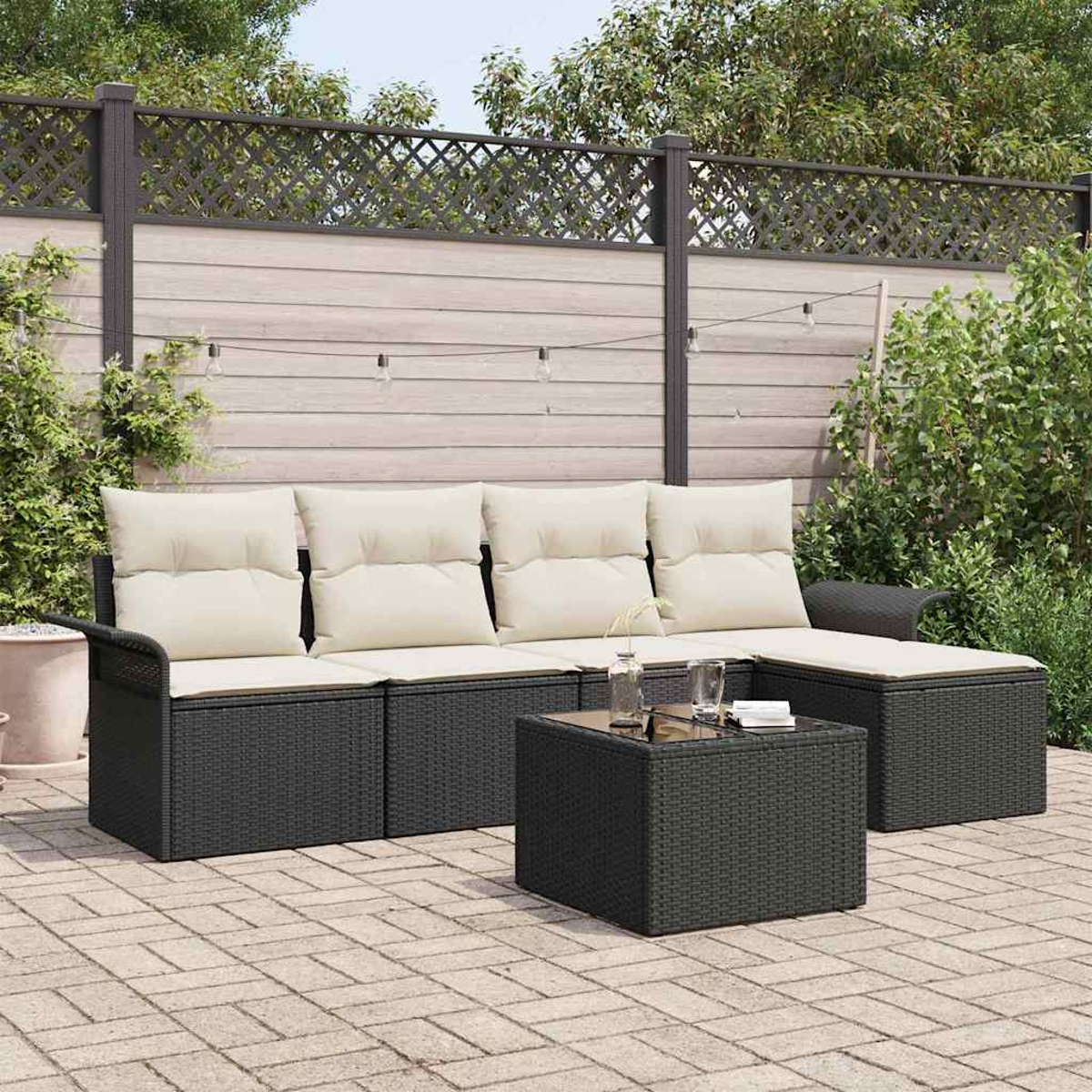 Garten-Lounge-Set mit schwarzen Möbeln und cremefarbenen Kissen. Davor steht ein kleiner Tisch. Im Hintergrund ein Holzzaun.