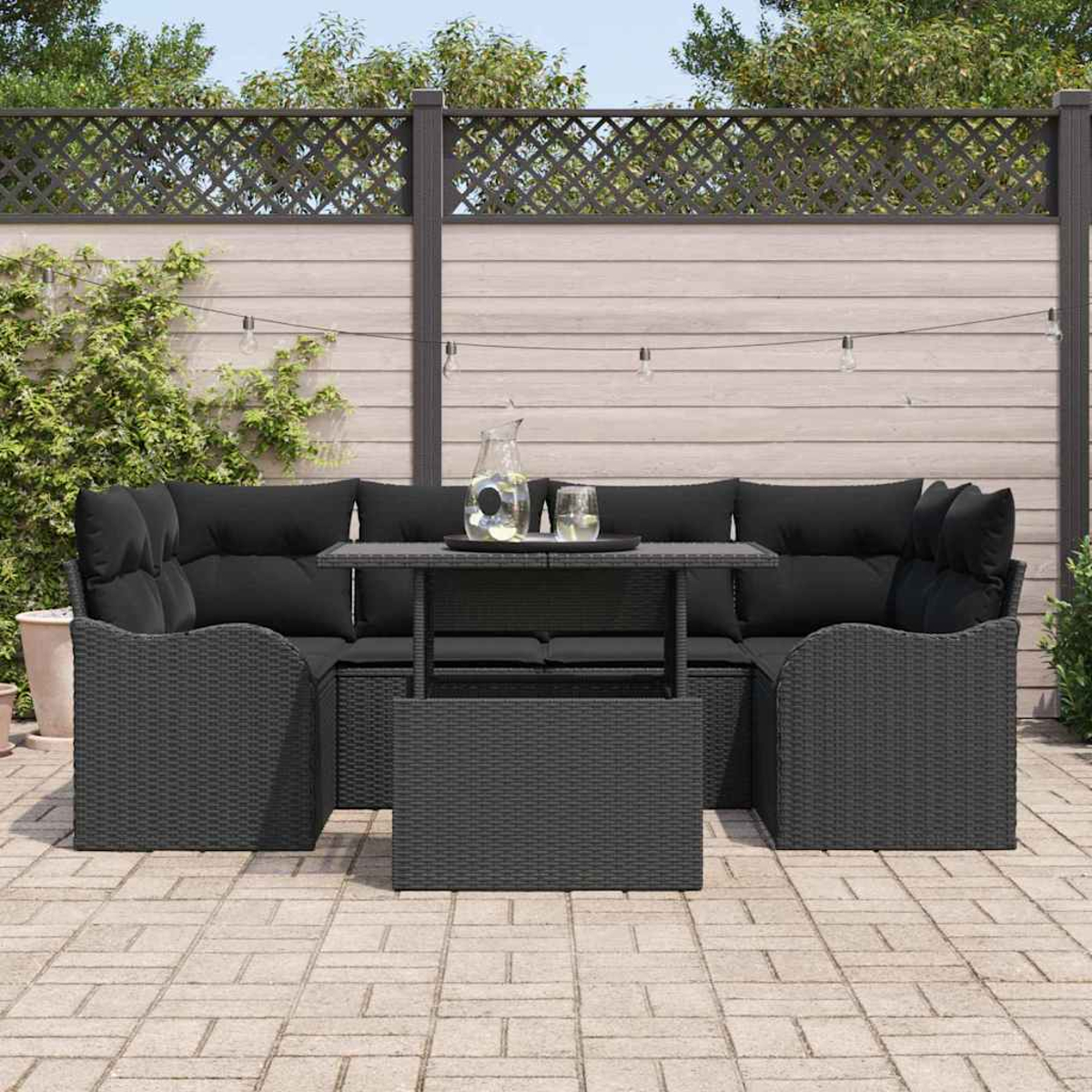 Outdoor-Terrassenset: dunkelgraue Korbmöbel mit schwarzen Kissen. Enthält einen Tisch und eine Kulisse aus Zaun und Grün.