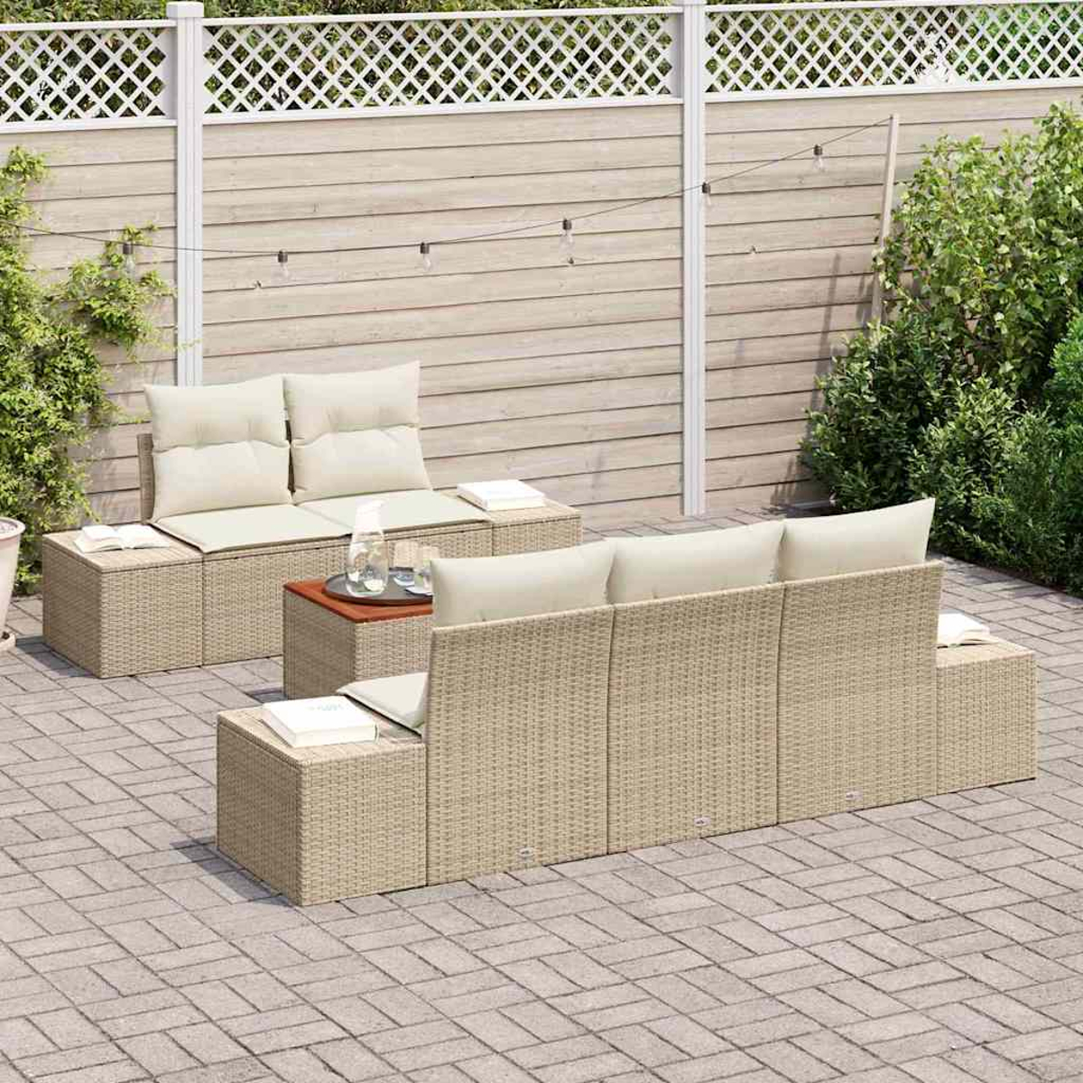 Terrassenmöbel-Set mit beigen Korbmöbeln, cremefarbenen Kissen und einem Holztisch auf einer Ziegelterrasse. Ein Holzzaun und Grün im Hintergrund.