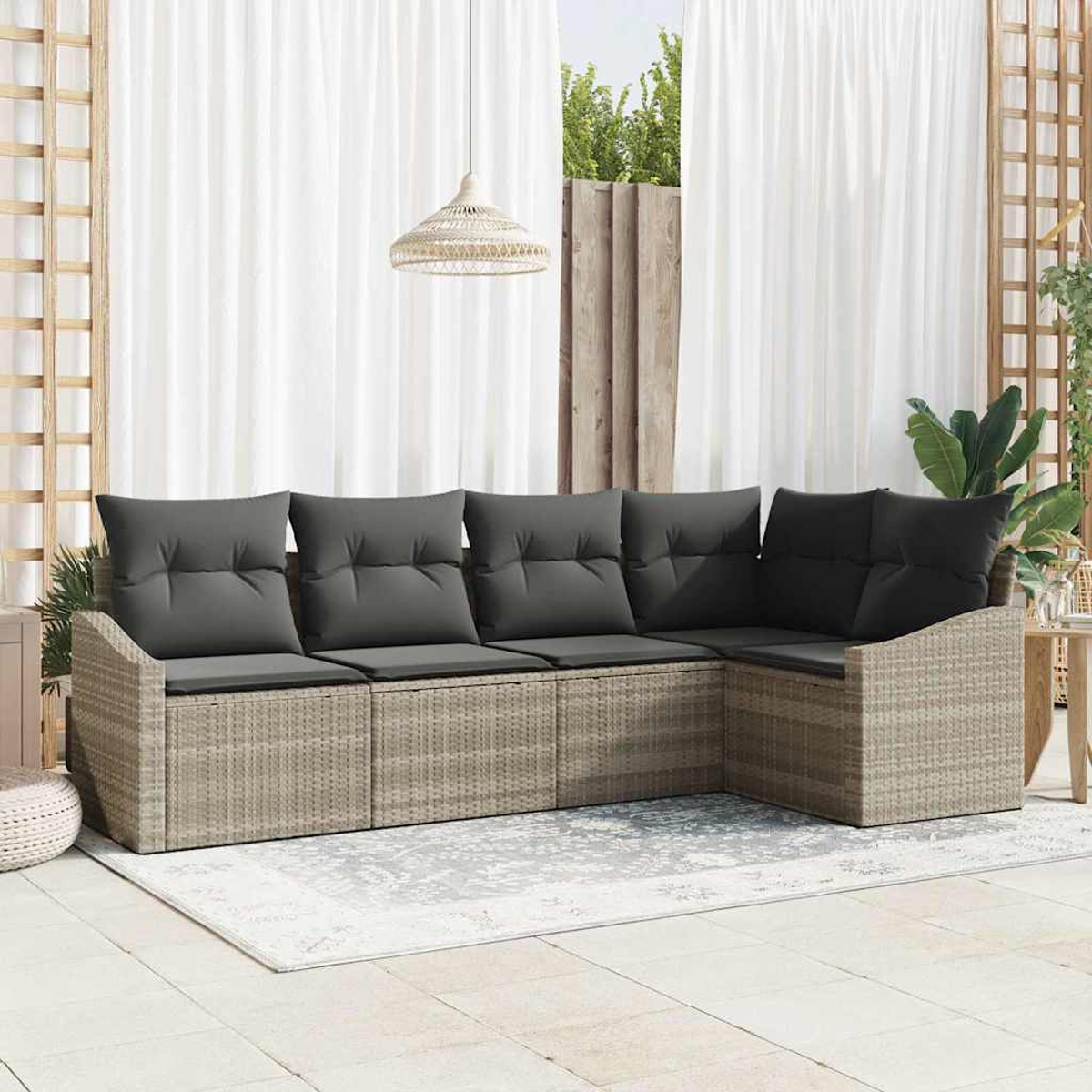 Ein Ecksofa aus Korbgeflecht mit grauen Kissen steht auf einer Terrasse. Im Hintergrund befinden sich weiße Vorhänge, und eine Leuchte hängt darüber.