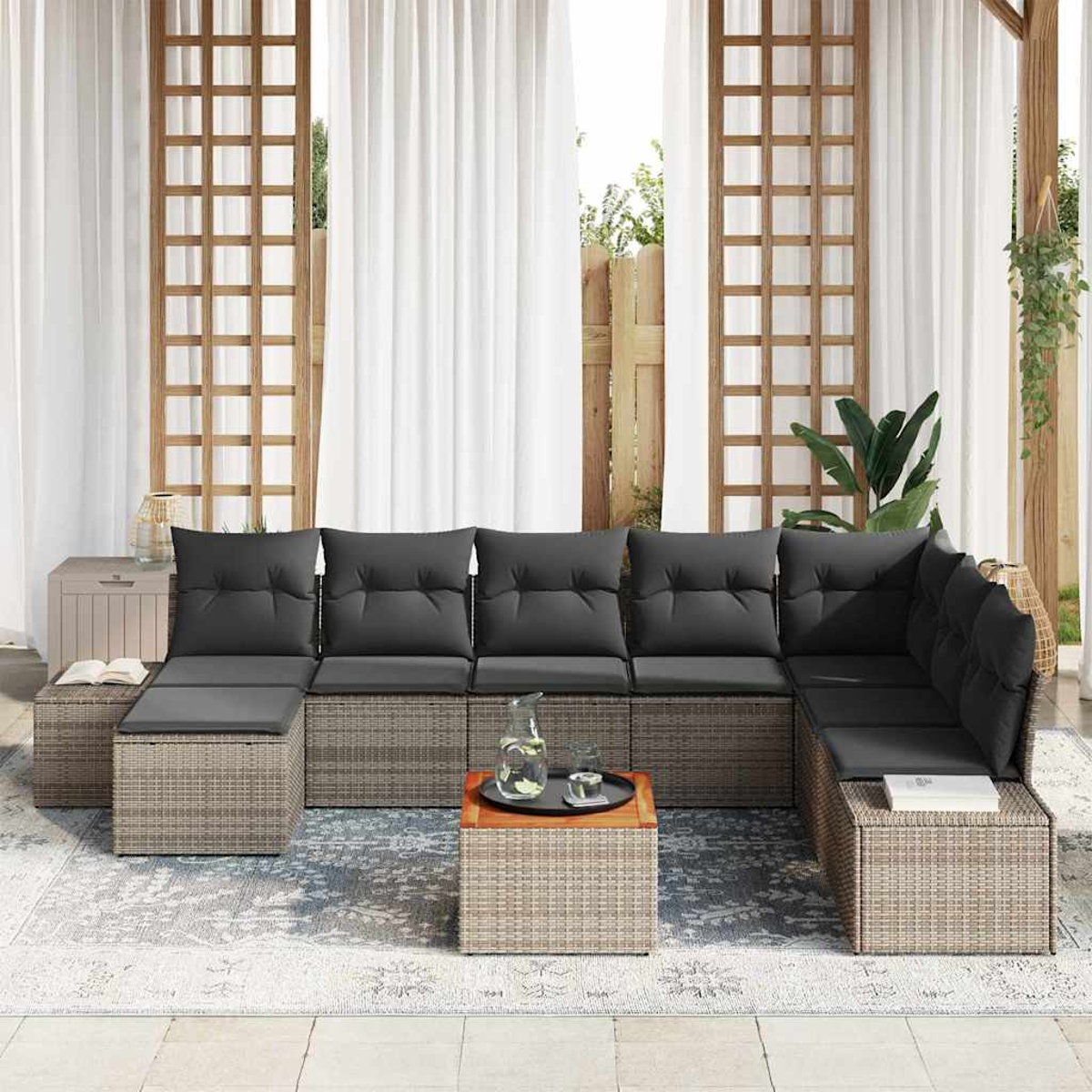 Outdoor-Ecksofa mit grauen Kissen auf einem gemusterten Teppich. Tisch mit Getränken davor. Vorhänge und Holzgitter im Hintergrund.