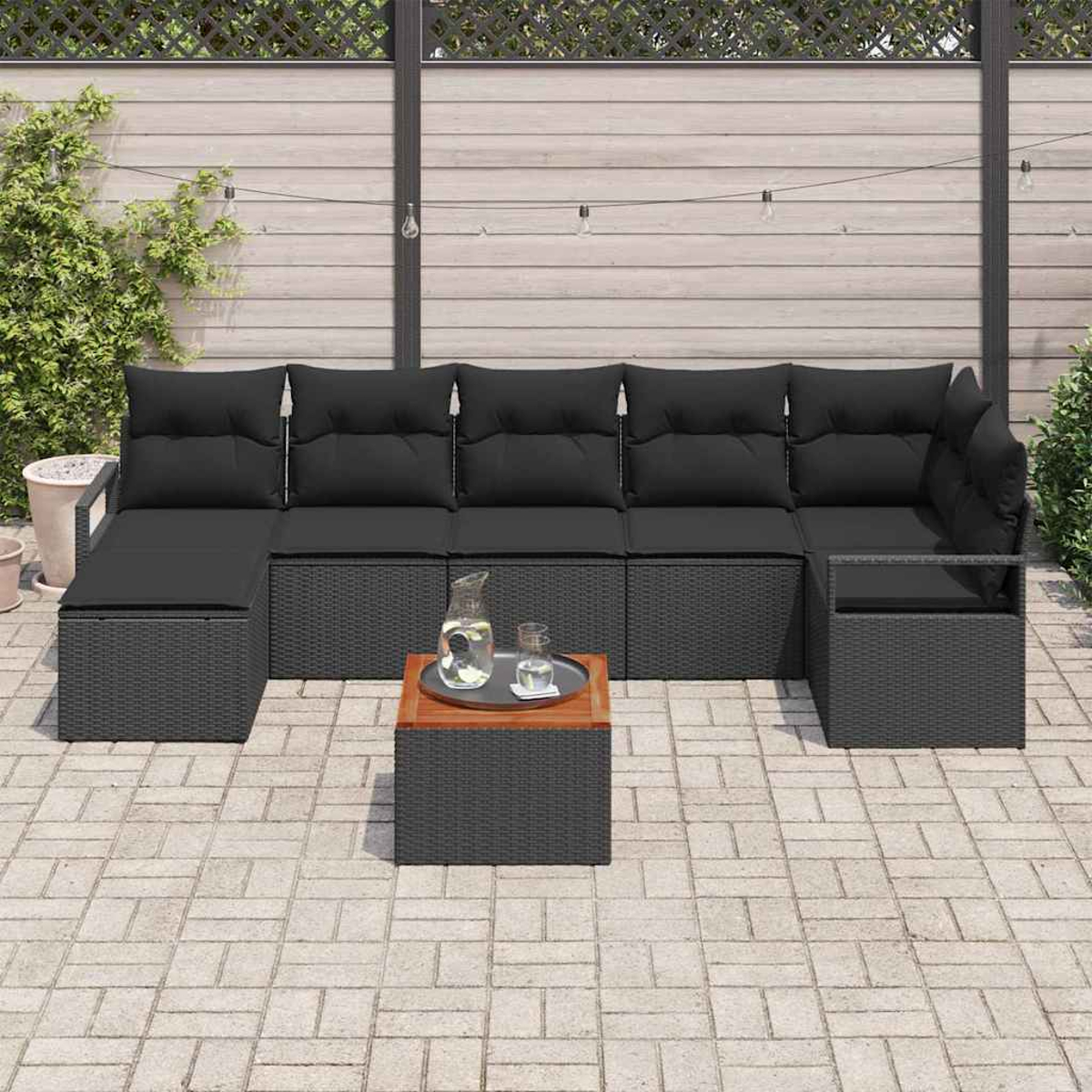Schwarzes Outdoor-Rattan-Ecksofa mit schwarzen Kissen, ein kleiner Tisch mit Tablett und Getränken auf einer gepflasterten Terrasse.