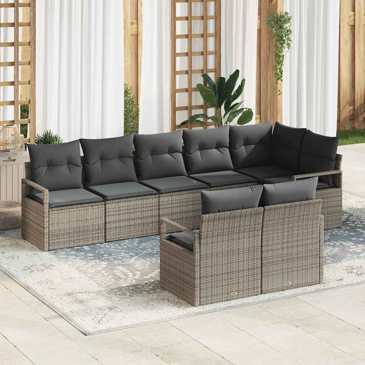 Garten-Wickersofa-Set mit grauen Kissen auf einem gemusterten Teppich. Weiße Vorhänge und Holzgitter im Hintergrund.