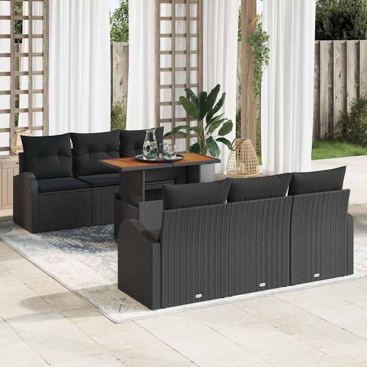 Terrassenset mit schwarzem Korbmöbel, Tisch, Kissen, auf einem Teppich. Weiße Vorhänge und Pflanzen im Hintergrund.