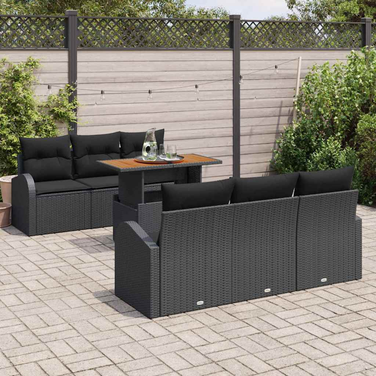 Terrassenset mit schwarzen Kissen. Enthält einen Tisch mit Gläsern und einer Kanne. Die Szene spielt in einem Hinterhof.