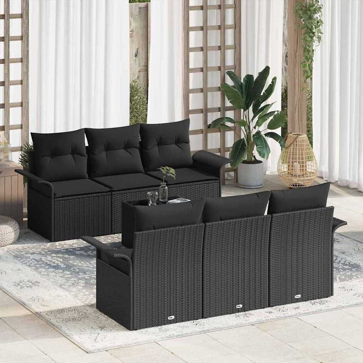 Szene im Freien mit schwarzen Korbmöbeln. Zwei Sofas, ein Couchtisch und dekorative Elemente wie eine Pflanze und eine Laterne sind sichtbar.
