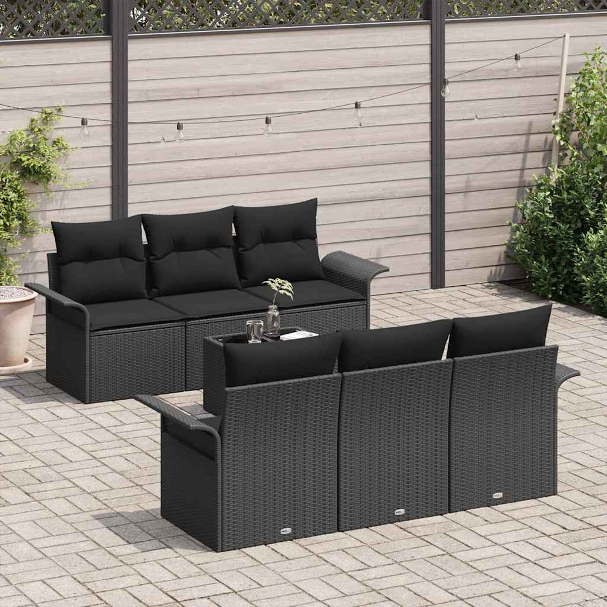 Zwei schwarze Korbsessel mit schwarzen Kissen stehen auf einer Terrasse. Ein kleiner Tisch steht dazwischen. Der Hintergrund zeigt einen Holzzaun.