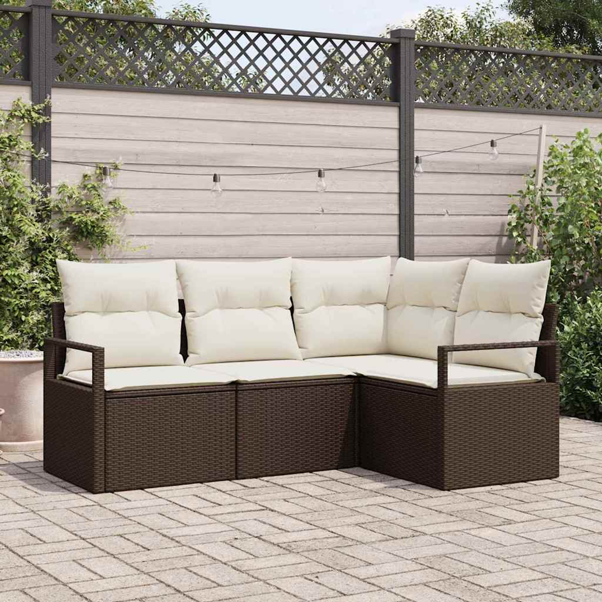 Un sofá seccional de ratán marrón con cojines crema en un patio. Una valla con celosía decorativa está detrás del sofá. Luces de cadena arriba.