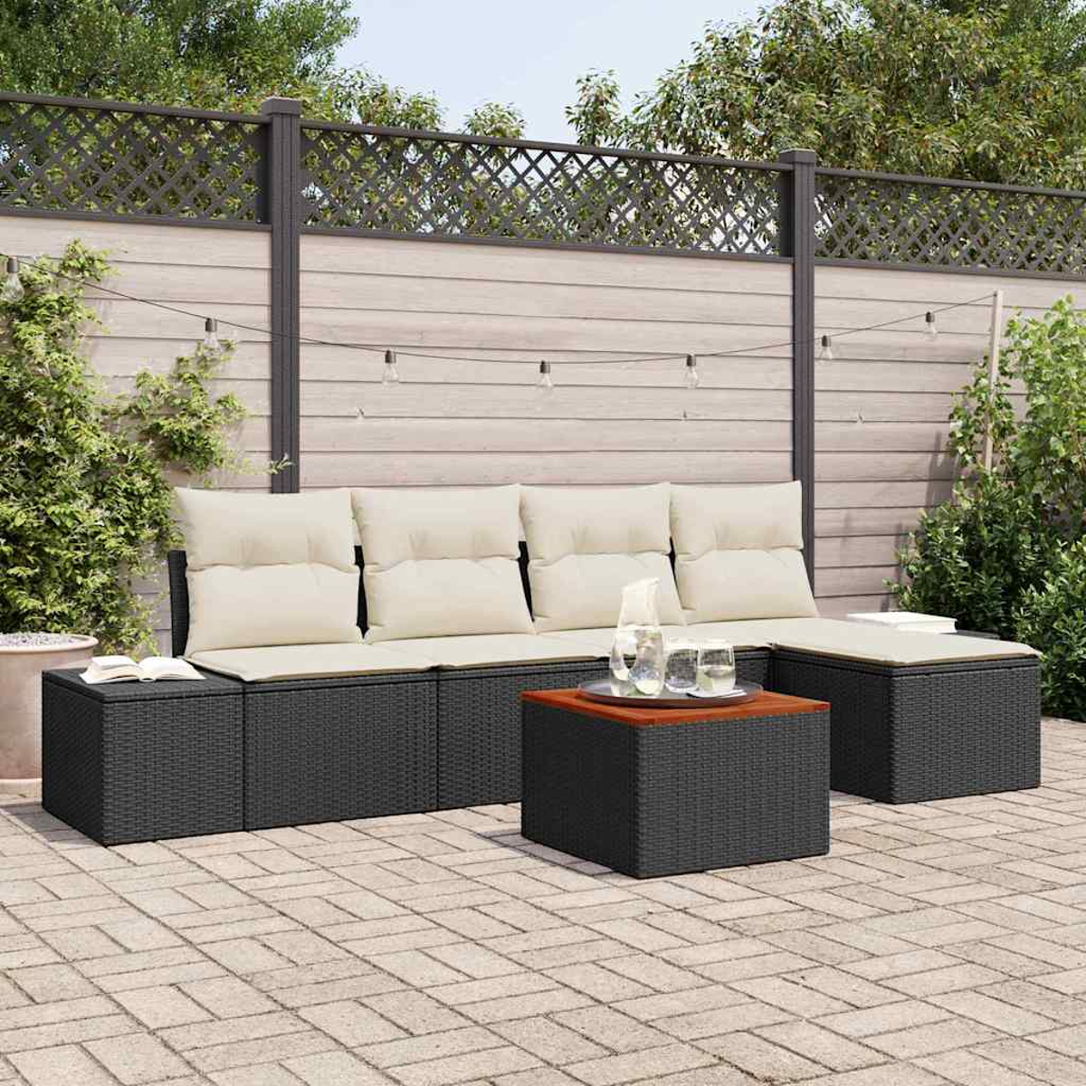 Gartenmöbel mit schwarzem Korbmöbel, beigen Kissen und einem Tisch mit Holzplatte. Im Hintergrund ein Holzzaun und Grün.
