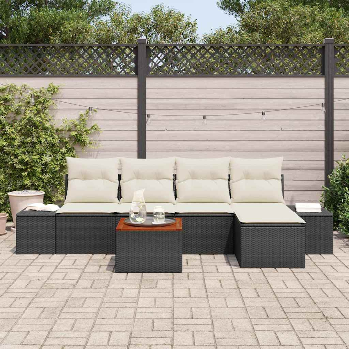 Gartensektionssofa mit cremefarbenen Kissen, kleiner Holztisch mit Glas und Krug, auf einer Ziegelterrasse, mit Zaun im Hintergrund.