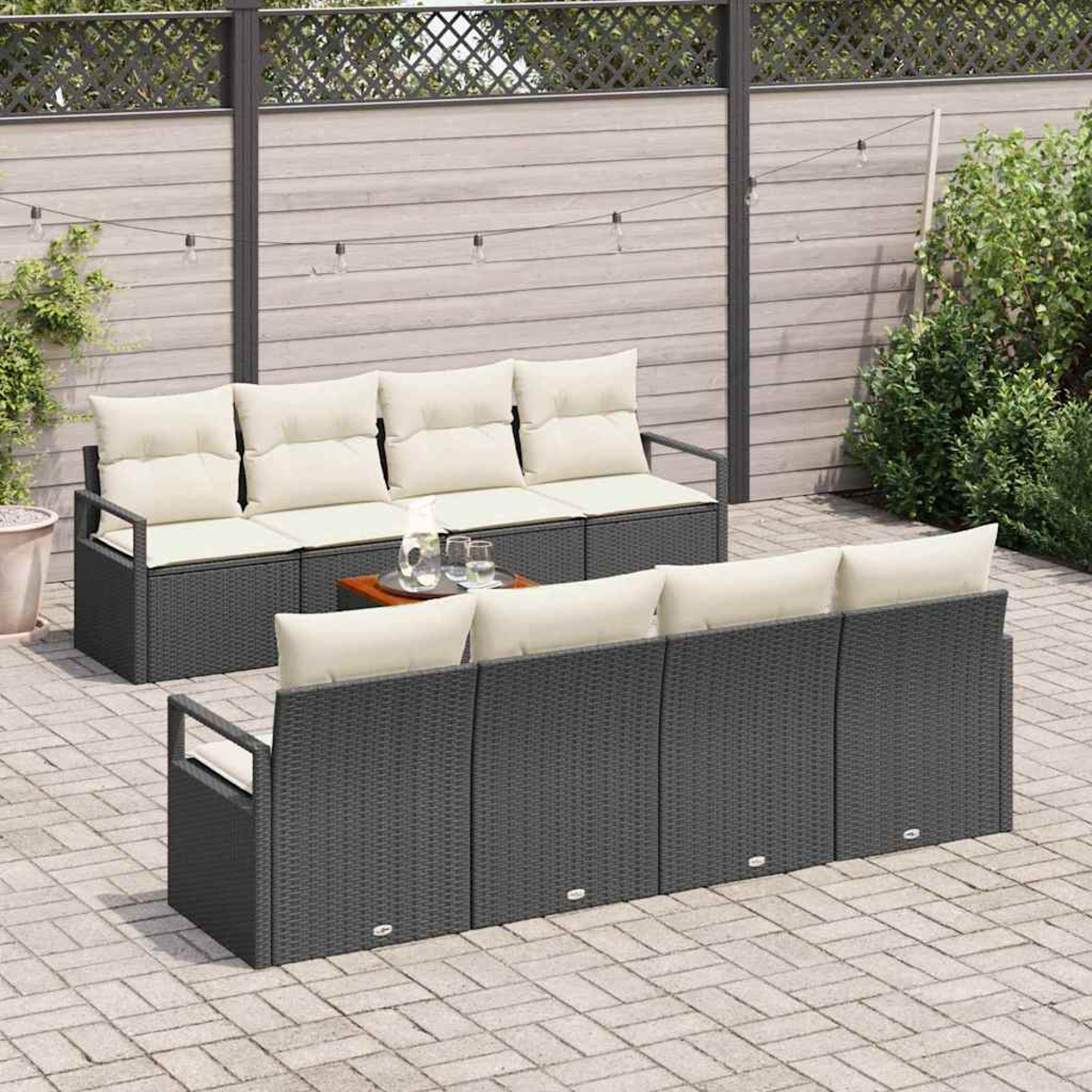 Garten-Set mit dunkelgrauen Korbsesseln, cremefarbenen Kissen, kleinem Tisch mit Gläsern, auf einer Backstein-Terrasse, Holzzaun im Hintergrund.