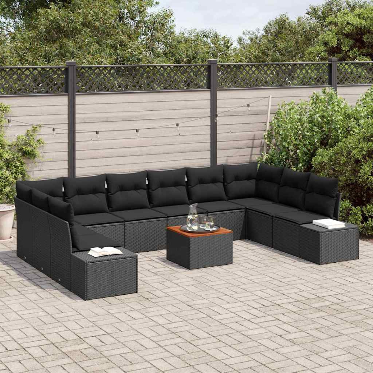 Outdoor-Ecksofa mit schwarzen Kissen, einem Holztisch und einer Steinterrasse. Ein Zaun und Grün bilden den Hintergrund.