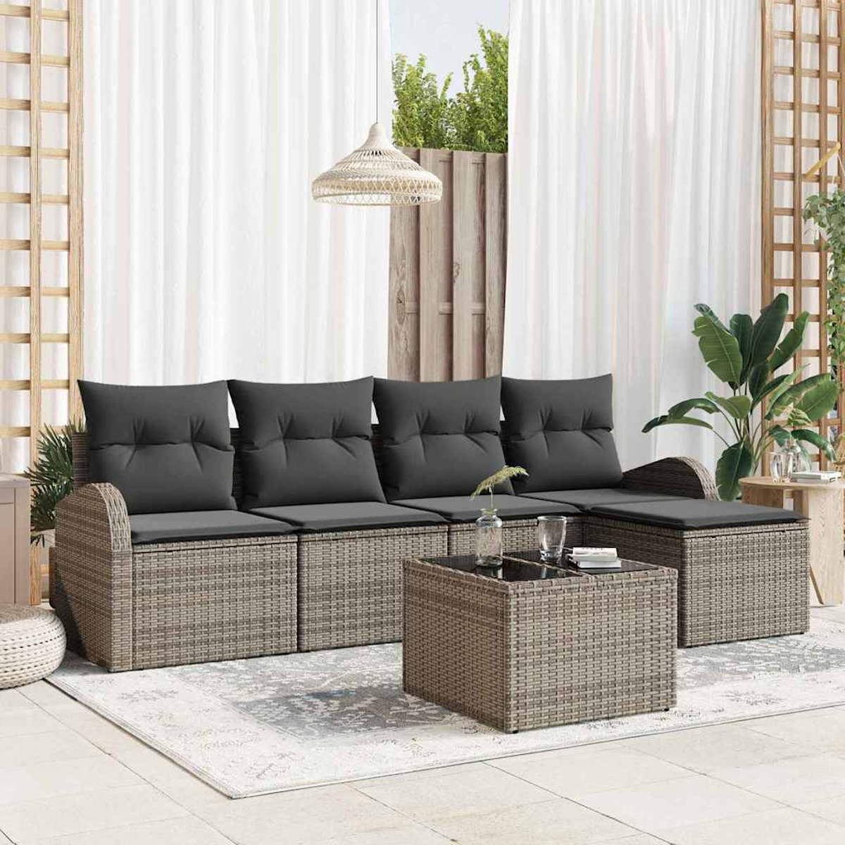 Garten-Sitzgruppe mit grauen Kissen und einem Tisch mit Glasplatte auf einem Teppich. Weiße Vorhänge im Hintergrund. Pflanzen und eine Hängelampe.