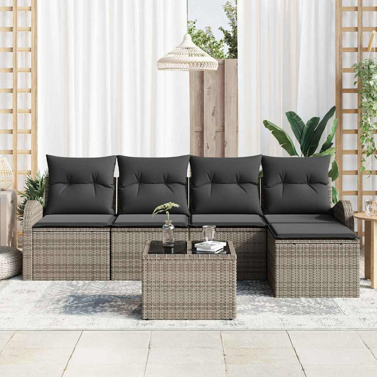Gartenmöbel-Set aus Korbgeflecht mit grauen Kissen, einem Tisch mit Glasplatte und weißen Vorhängen.