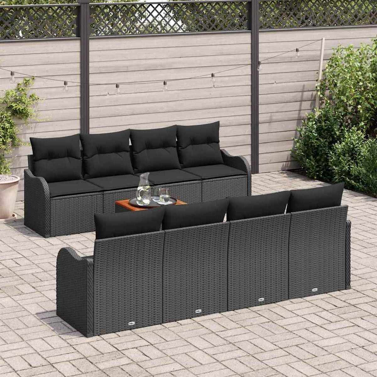 Terrassenmöbel-Set mit grauen Korbsesseln, schwarzen Kissen, kleinem Tisch mit Getränken und Holzzaun im Hintergrund.