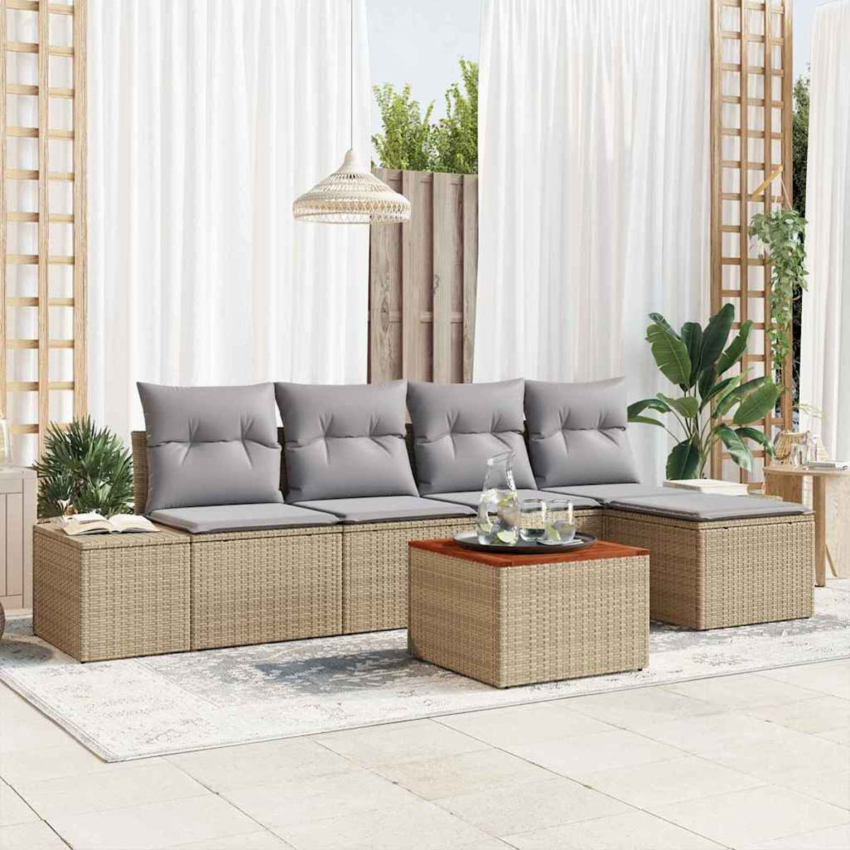 Zona de estar al aire libre con muebles de mimbre, cojines grises y una mesa de madera. Cortinas blancas y plantas en el fondo.