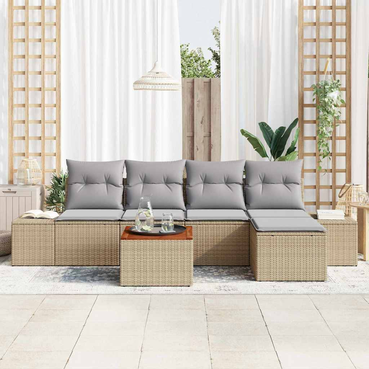 Zona de estar al aire libre con muebles de mimbre, cojines grises y una mesa de madera. Cortinas blancas y enrejado con plantas en el fondo.
