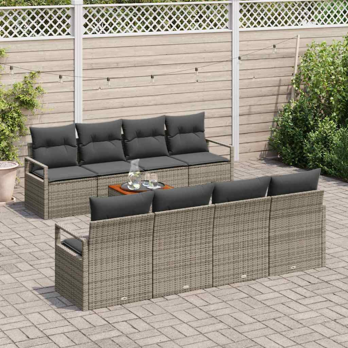 Terrassenmöbel-Set mit grauem Korbmöbel und Kissen, einem kleinen Tisch mit Getränken und einem Holzzaun im Hintergrund.