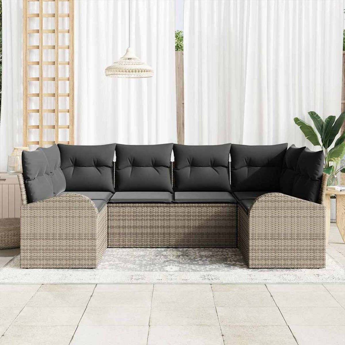 Ein geflochtenes Outdoor-Ecksofa mit grauen Kissen steht auf einem Teppich. Weiße Vorhänge und eine Hängeleuchte sind im Hintergrund.