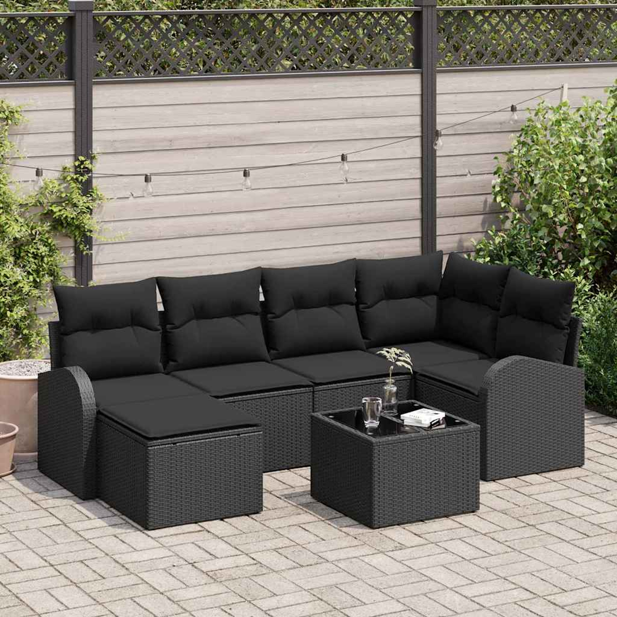 Schwarzes Outdoor-Rattan-Sofa-Set mit Kissen und kleinem Tisch auf einer gepflasterten Terrasse. Ein Zaun und Grün im Hintergrund.