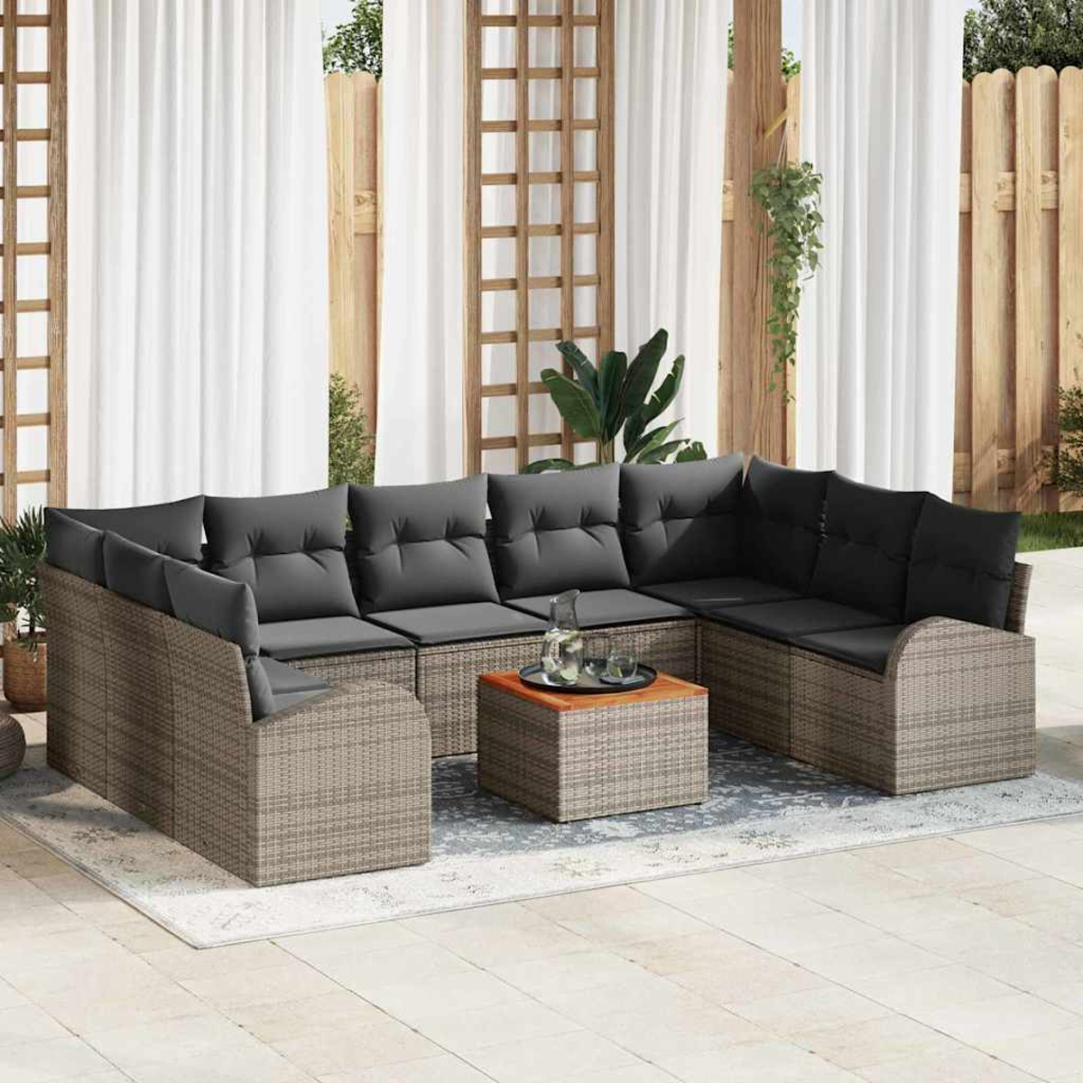 Sofá seccional para exteriores con cojines grises, mesa de madera pequeña con bandeja y cortinas blancas al fondo.