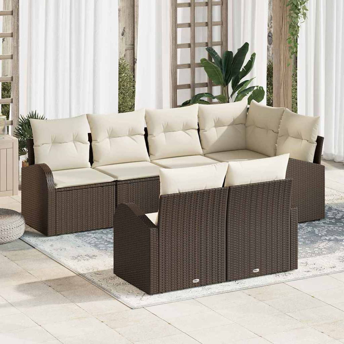 Sofá seccional exterior con cojines crema. Marcos de mimbre marrón. Cortinas blancas y plantas al fondo.