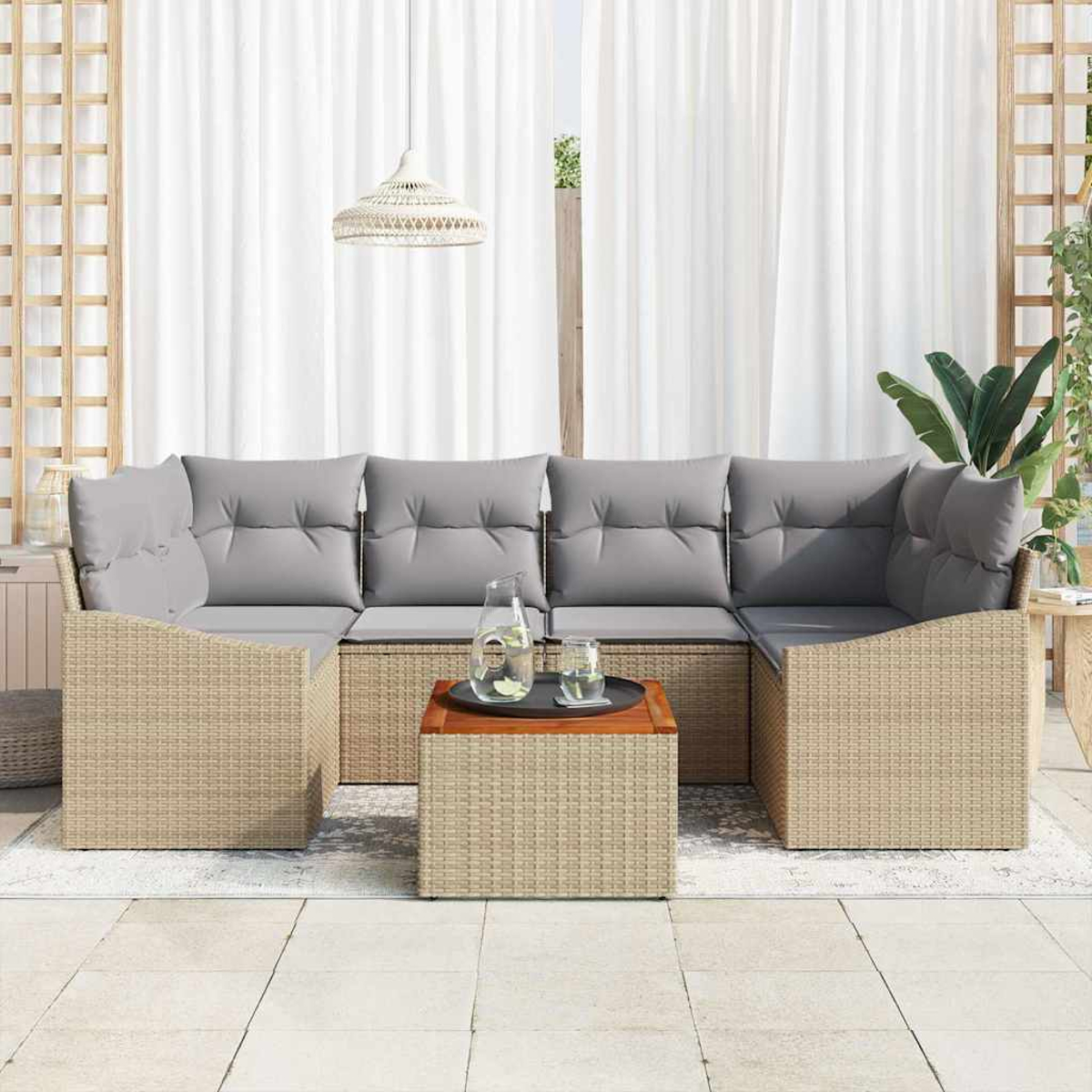 Garten-Sitzgruppe mit grauen Kissen und einem Rahmen aus gewebtem Rattan. Ein Tisch mit Wasser und eine Lampe vor weißen Vorhängen.