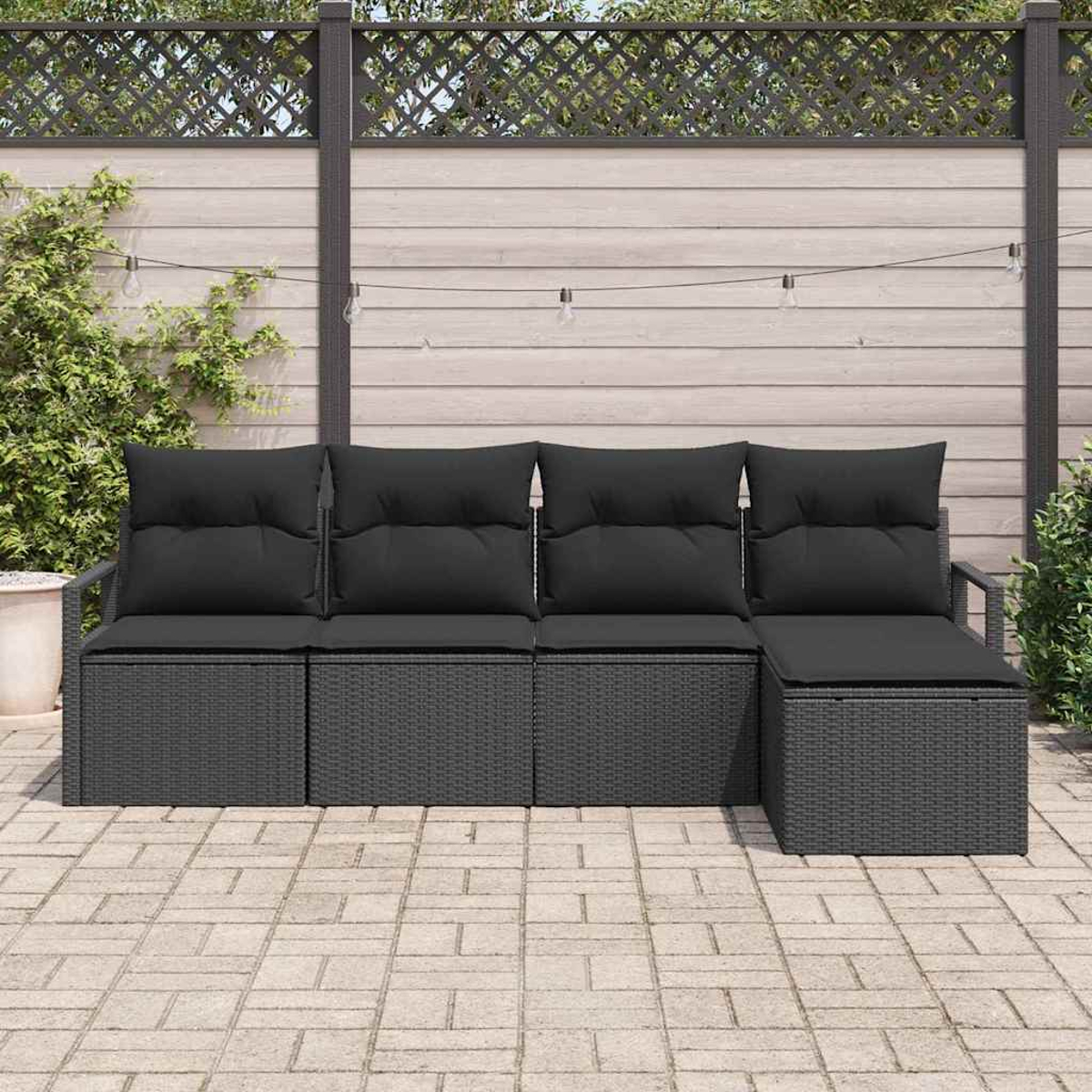 Ein graues Outdoor-Sofa mit schwarzen Kissen steht auf einer Terrasse. Im Hintergrund ist ein Holzzaun mit einem Gitter.