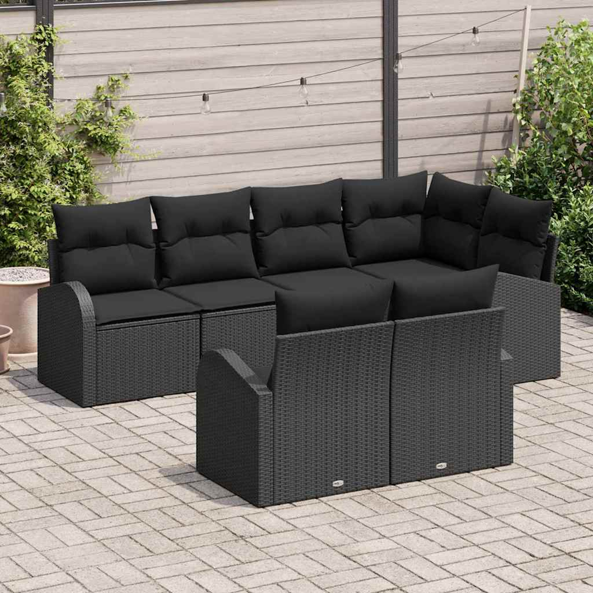 Outdoor-Ecksofa mit schwarzen Kissen auf einer Steinterrasse. Im Hintergrund ein Holzzaun mit einigen Pflanzen.