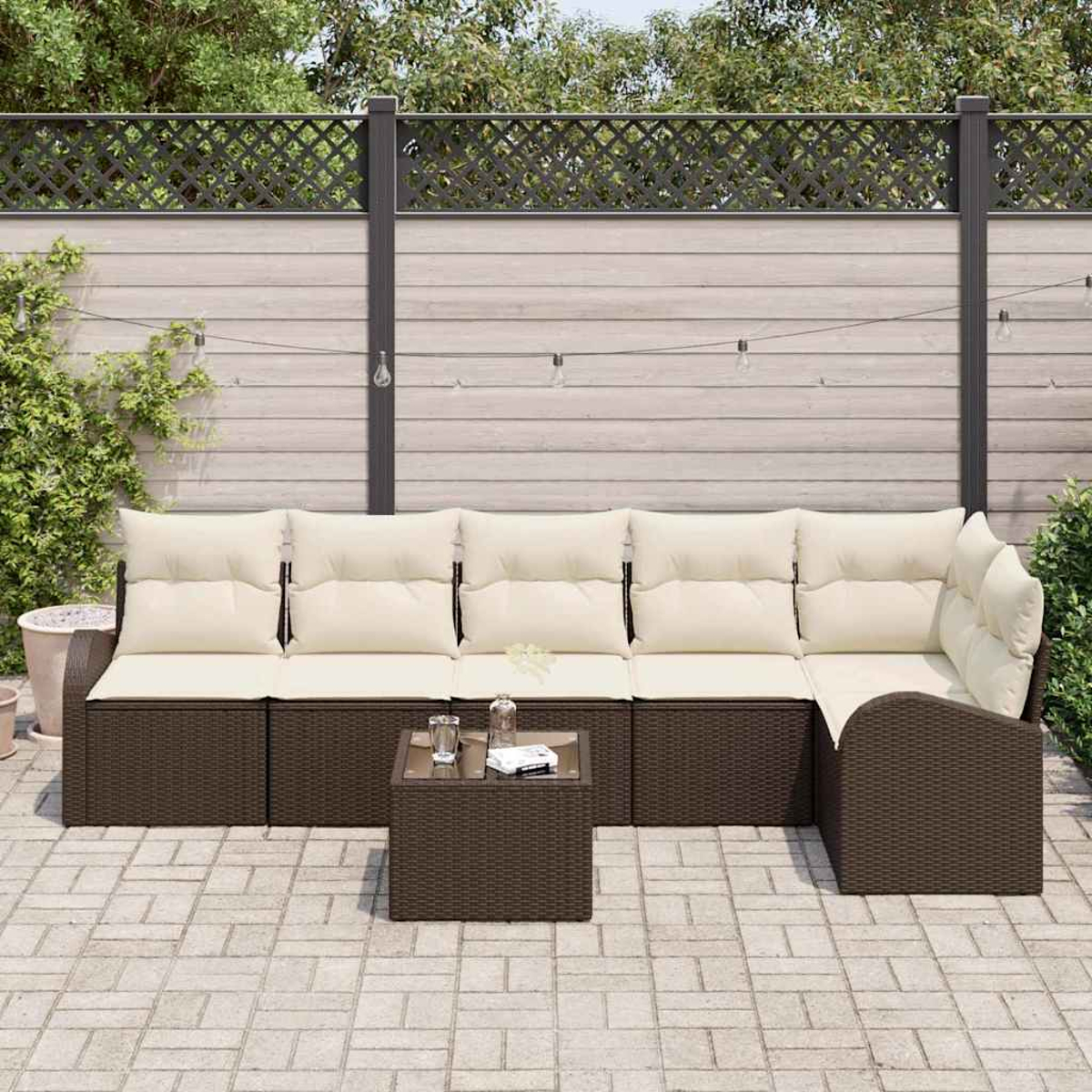Outdoor-Ecksofa mit cremefarbenen Kissen und einem kleinen Tisch. Braune Korbmöbel stehen auf einer Terrasse mit Zaun im Hintergrund.
