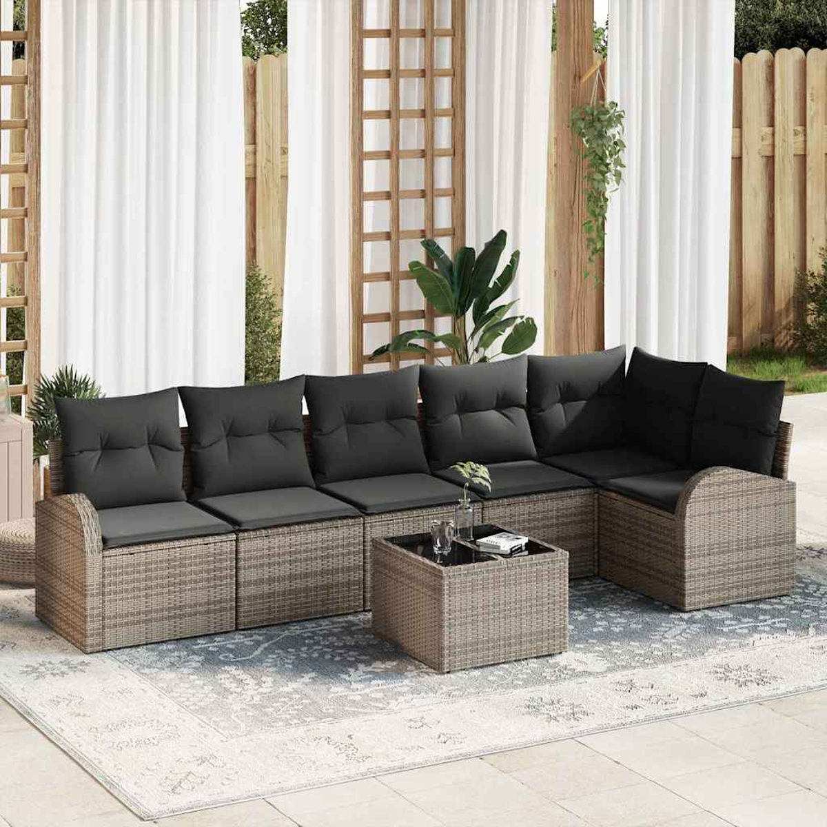 Gartenlounge mit grauen Kissen, kleinem Tisch und Teppich. Weiße Vorhänge und Holzgitter im Hintergrund.