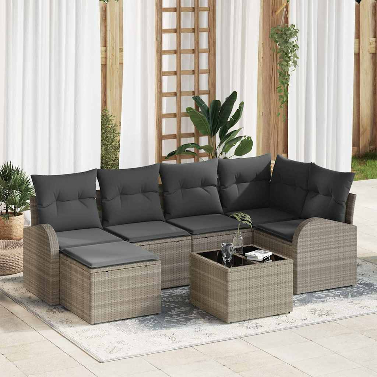 Outdoor-Rattan-Ecksofa mit grauen Kissen, einem Couchtisch und Pflanzen. Im Hintergrund weiße Vorhänge und Holzstruktur.