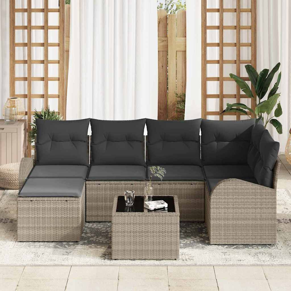 Outdoor-Ecksofa mit grauen Kissen und einem kleinen Tisch. Fenster und Vorhänge sind im Hintergrund. Rechts ist eine Pflanze.