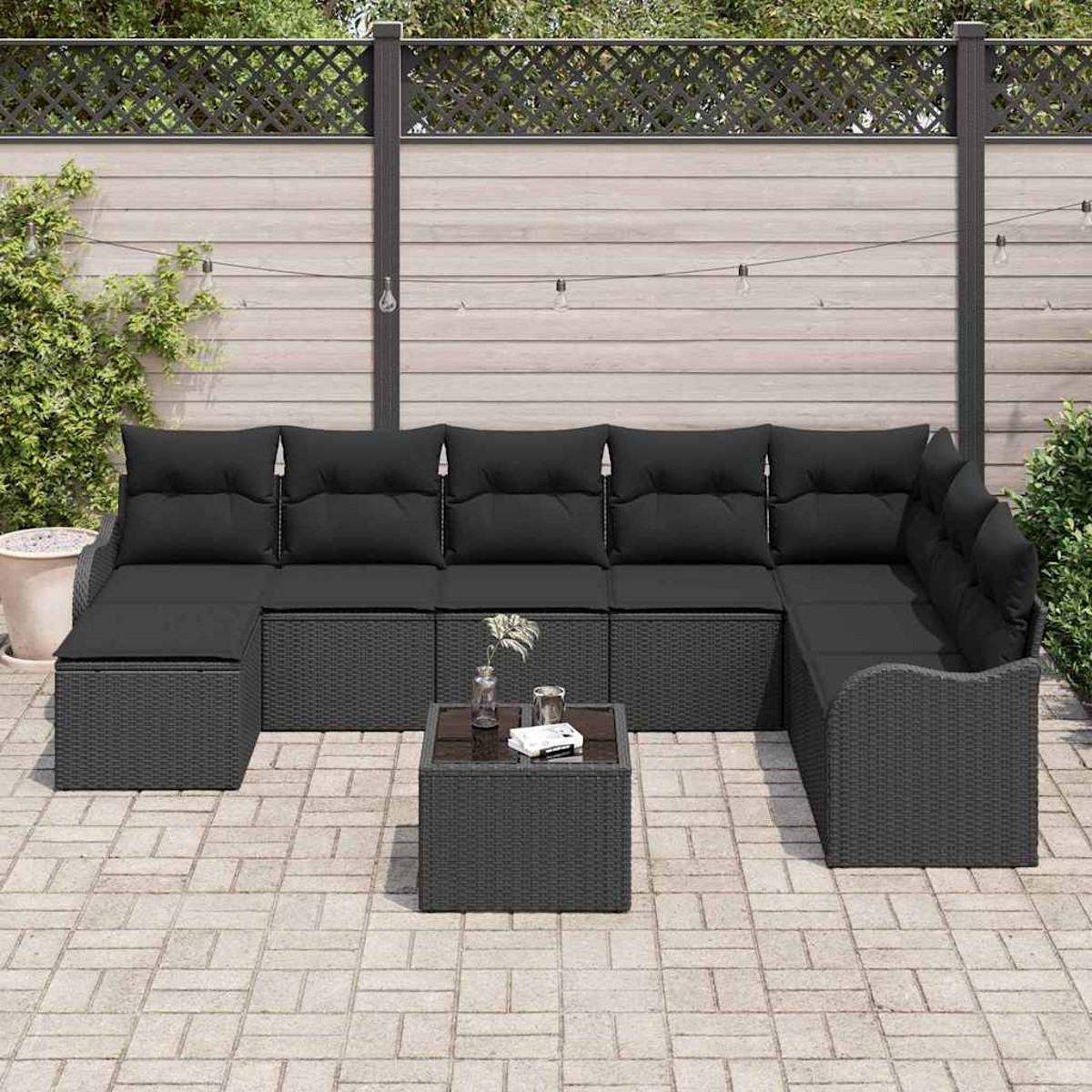 Outdoor-Ecksofa mit schwarzen Kissen und einem kleinen Tisch auf einer Steinterrasse. Im Hintergrund ein Zaun und Grün.