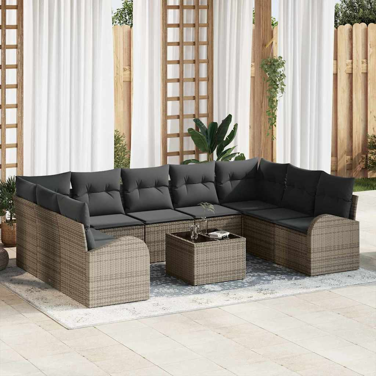 Outdoor-Ecksofa mit grauen Kissen und einem quadratischen Couchtisch auf einem Teppich. Weiße Vorhänge und Holzzaun im Hintergrund.