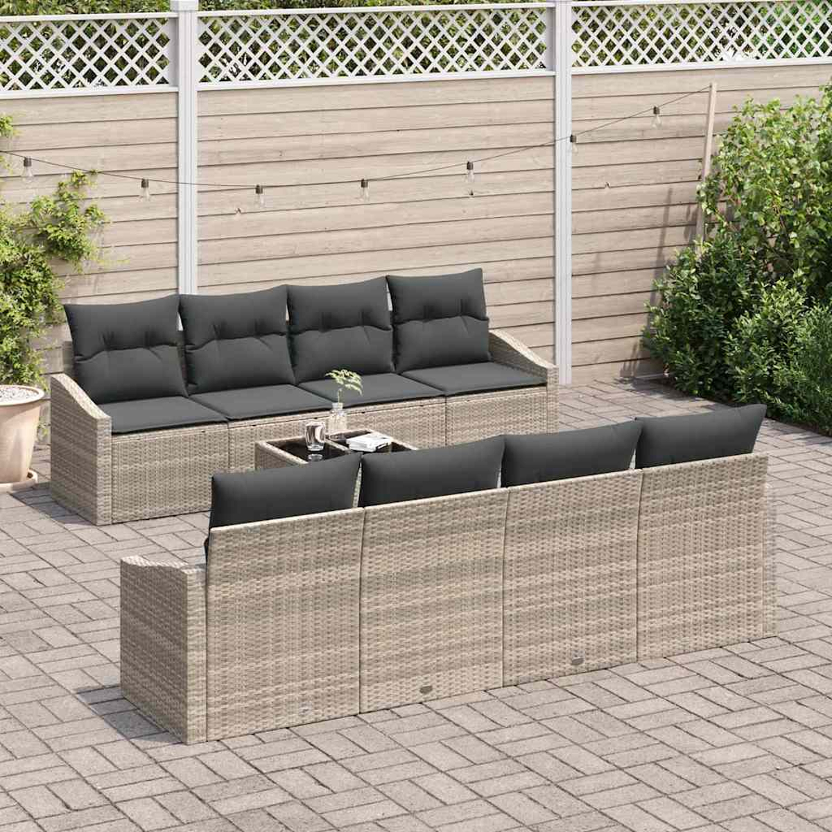 Garten-Terrassenset mit grauen Kissen. Korbmöbel auf einer gepflasterten Terrasse. Beinhaltet ein Sofa, eine Chaiselongue und einen Couchtisch.