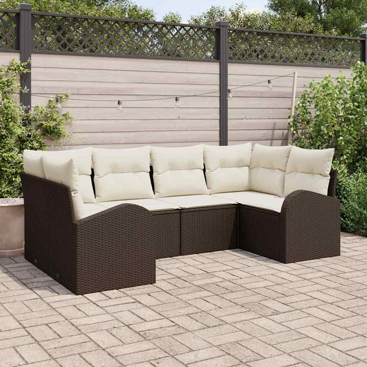 Outdoor-Ecksofa mit cremefarbenen Kissen und dunkelbraunem Korbgeflecht. Auf einer Terrasse mit Zaun im Hintergrund. Lichterketten sind oben.